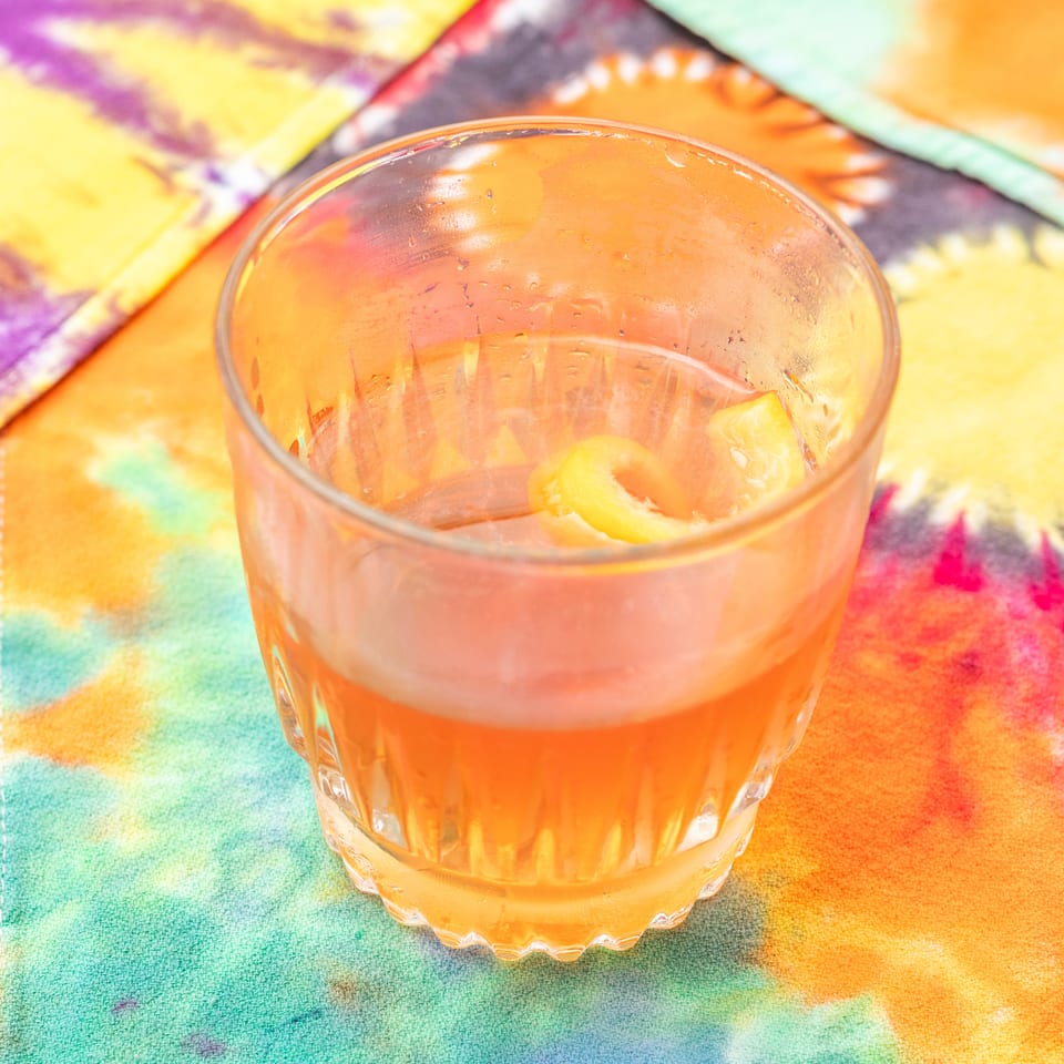 Orange beverage with citrus slices in a ridged glass on a colorful patterned tablecloth.