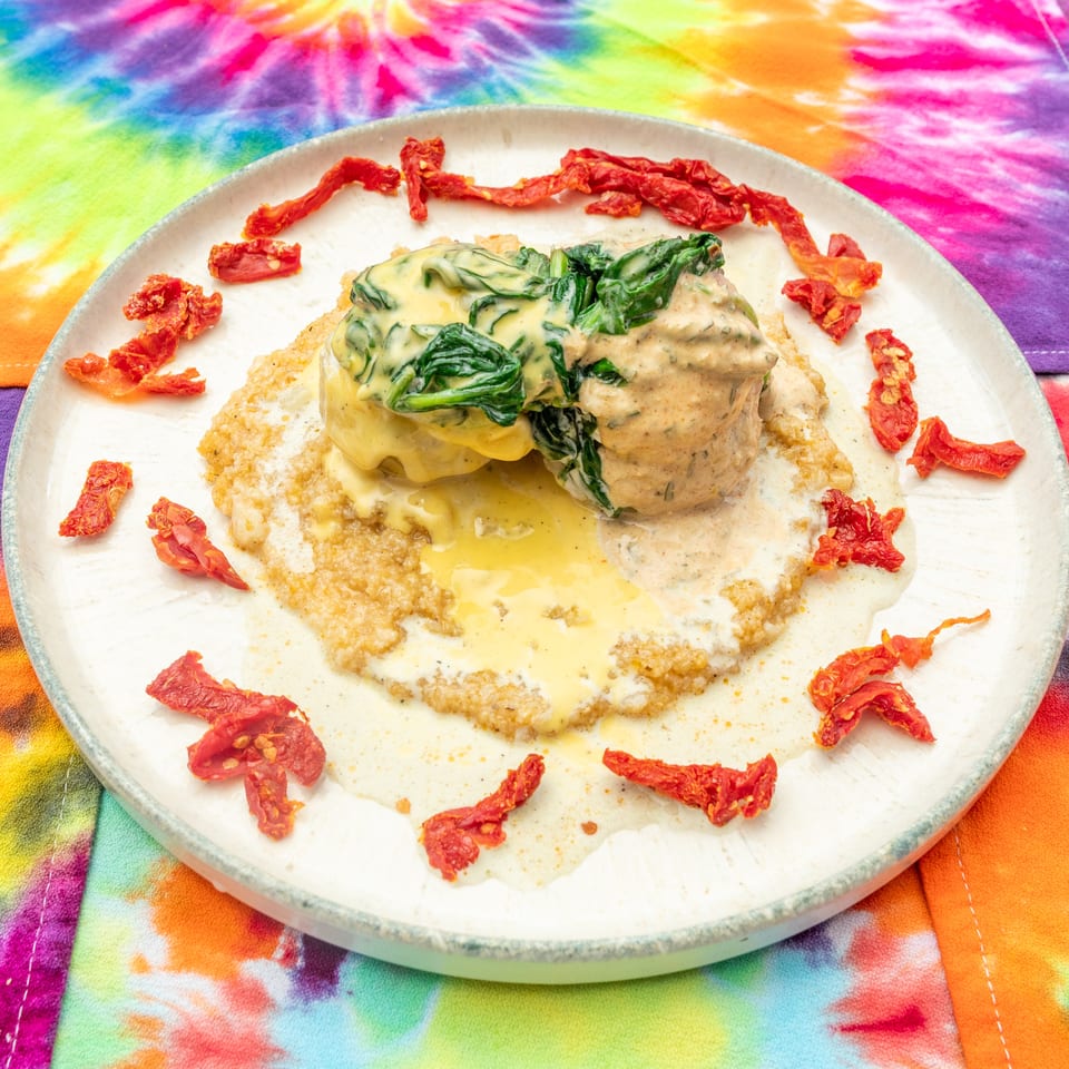 Creamy spinach-topped chicken over a crispy base, garnished with sun-dried tomatoes on a plate atop colorful tie-dye fabric.