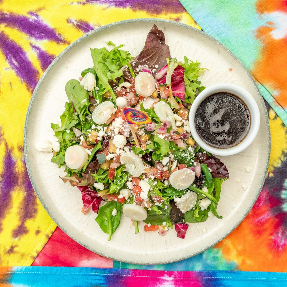 Colorful mixed green salad with vegetables, feta cheese, and dressing in a bowl on vibrant tie-dye fabric.