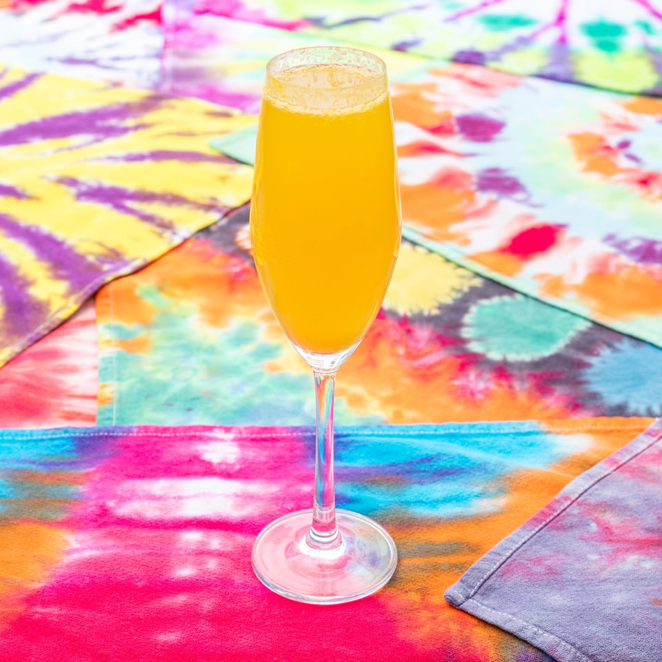 Golden beer served in a stemmed glass on a vibrant multicolored tie-dye tablecloth.