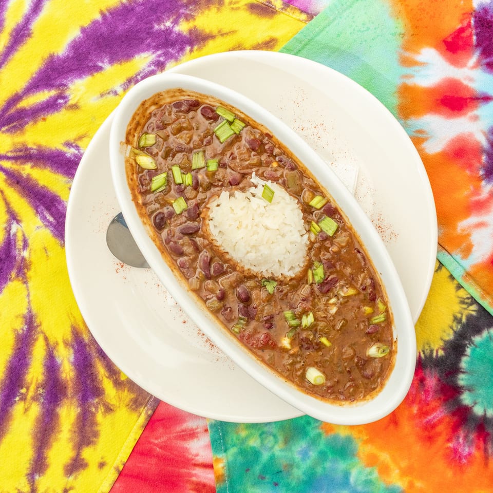 Bowl of red beans and rice garnished with green onions on a white plate, surrounded by colorful tie-dye fabric.