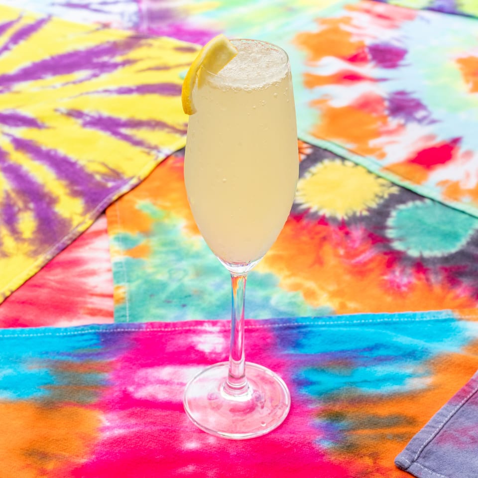 Frosted citrus cocktail in a stemmed glass garnished with lemon, set on a vibrant multicolored tablecloth.