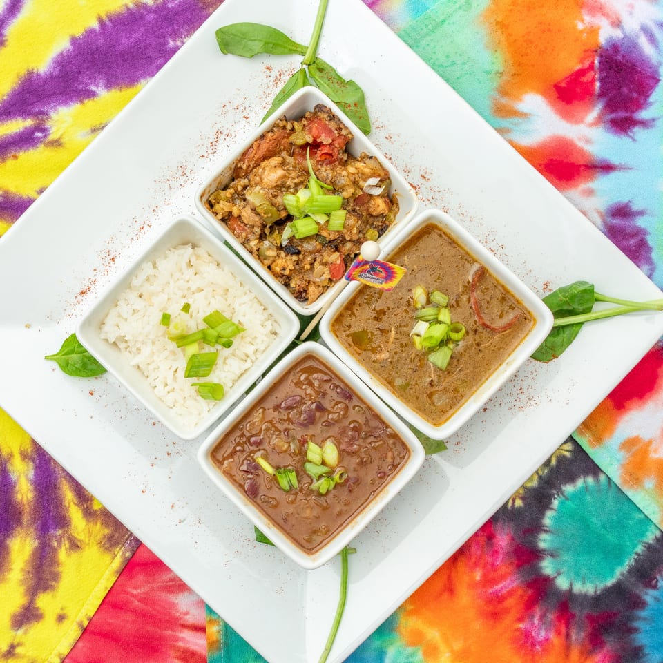 Assorted rice, beans, stewed meat, and sauces served in white bowls on a colorful tie-dye cloth.