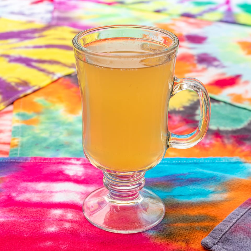 Glass mug filled with golden beverage on a vibrant multicolored patterned tablecloth.