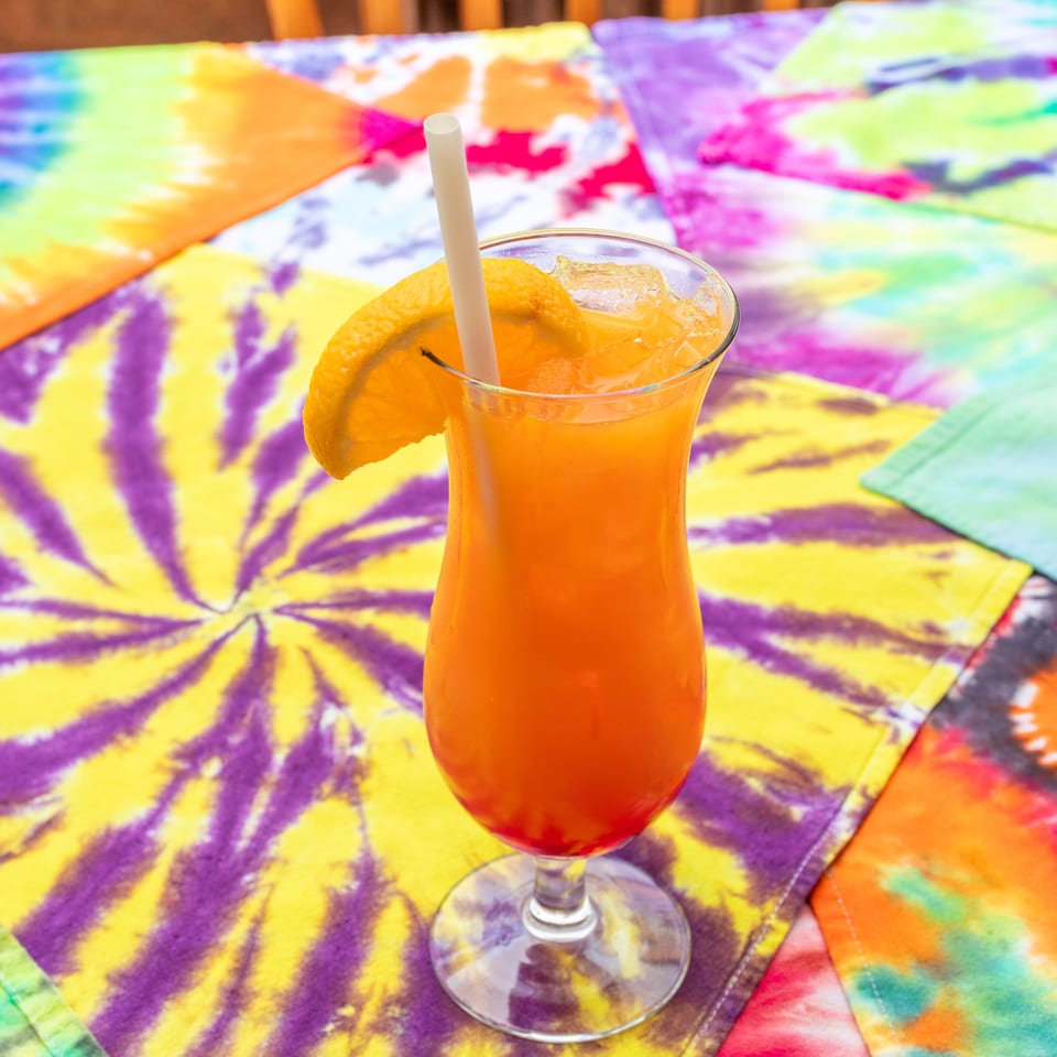 Orange cocktail with ice, straw, and citrus garnish on a vibrant multicolored patterned tablecloth.
